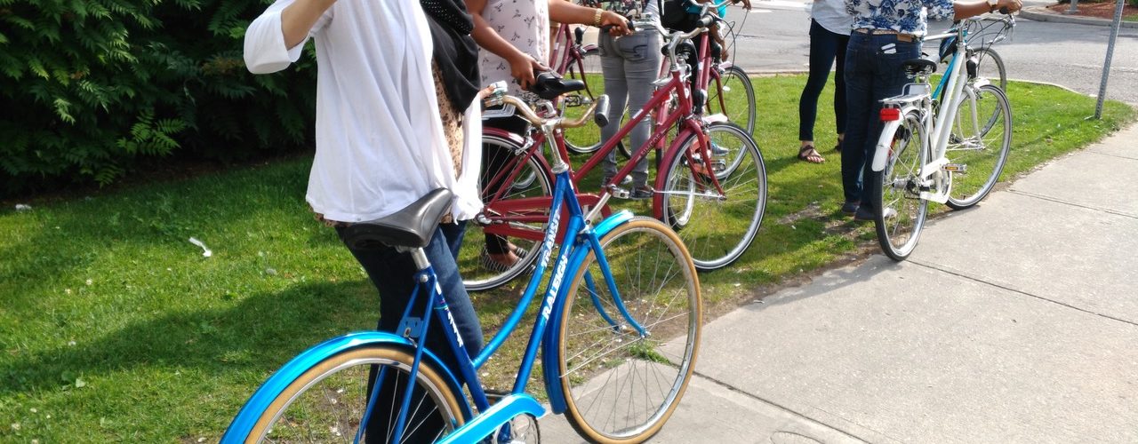 Image of a few people with bikes listening to a mentor on the side of the road.